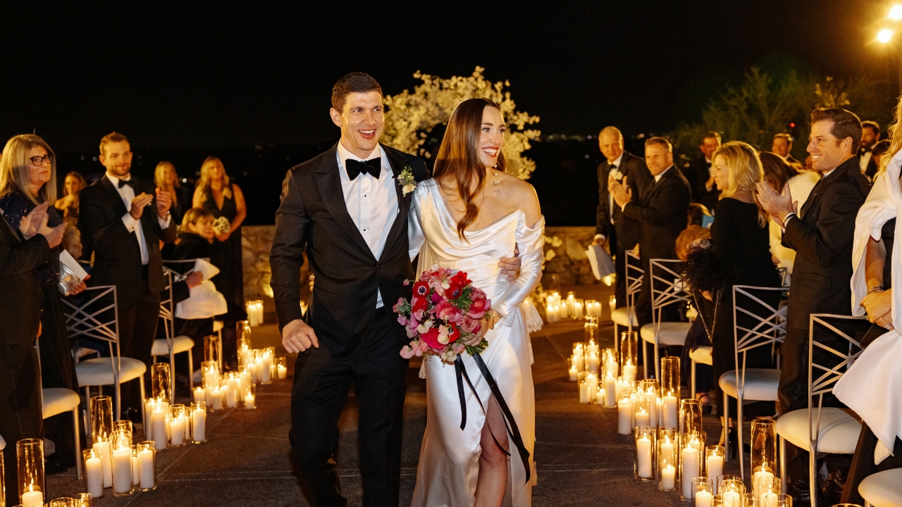 photo of bride and groom walking down the aisle surrounded by candles and guests at night