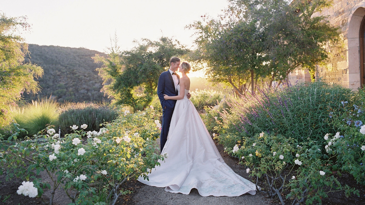 photo of bride and groom kissing in garden with sunsetting behind them