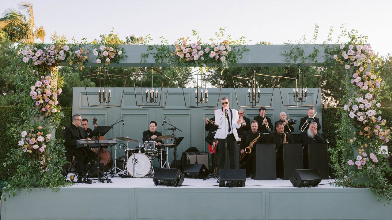 photo of band playing at wedding reception on green stage with floral accents